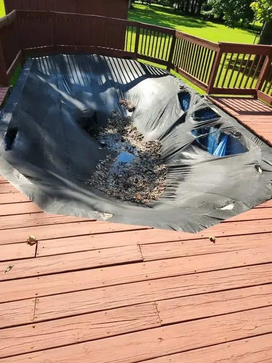 Above-ground pool on a backyard deck, covered with a torn tarp and full of leaves and standing water