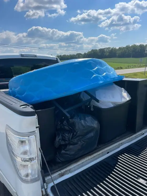 Pickup truck bed loaded with an inflatable pool, storage totes and bagged household junk
